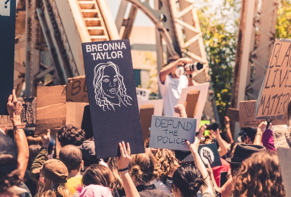 A photo of a Black Lives Matter protest from summer of 2020 featuring protestors holding signs that say "Black Lives Matter," "Breonna Taylor," and "Defund the Police"