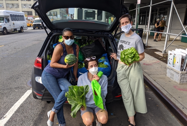 Leah and two other community members holding produce and posing in front of the open trunk of a car.