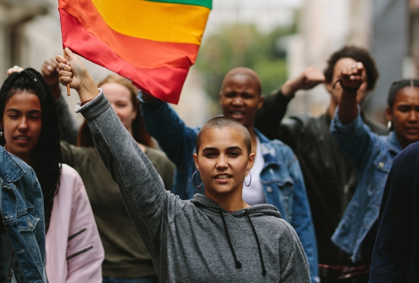young people of color and white passing people marching and waving LGBTQ+ flag