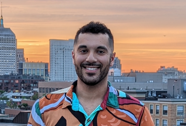photo of Ramy smiling with a city and sunset in the background