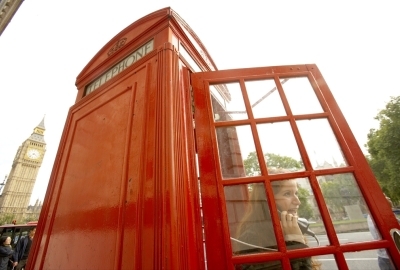 A person speaking on the phone in a red telephone booth.