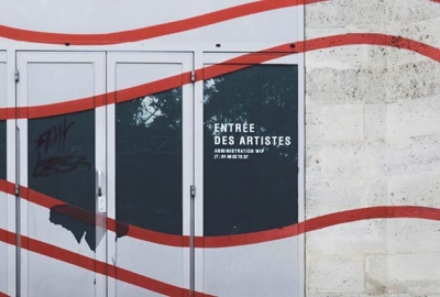 A wall with red squiggles painted over it and a doorway reading "Entree Des Artistes"