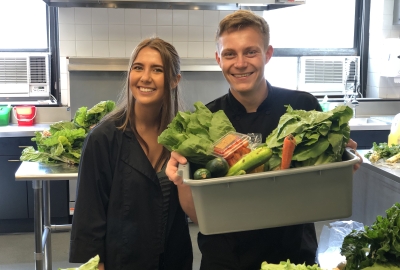 Two students holding a bucket of vegetables.