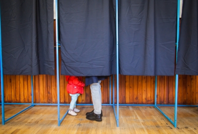 A photo of voting booths with the feet of a parent and child visible
