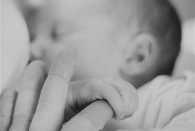 A tilt-shift photo of a breastfeeding child holding onto their mother's finger