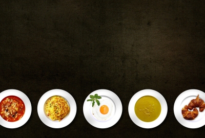 An overhead shot of various plates of pasta, eggs, soup, and croissants.