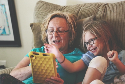 A woman and a young girl sit on a couch together and learn on a tablet