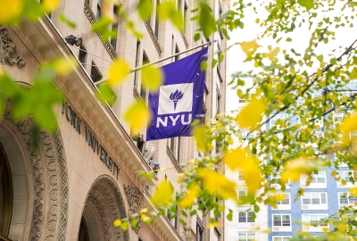 NYU flag on building with fall foliage in the foreground