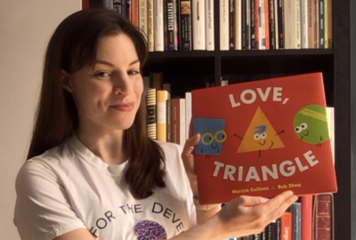 Dr. Moira Dillon holding up a book called "Love, Triangle" to read