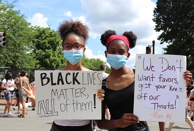 Two young black girls hold protest signs reading "Black Lives Matter, All of them!" and "'We Don't want favors, get your knee off our throats!' - Rev Al."