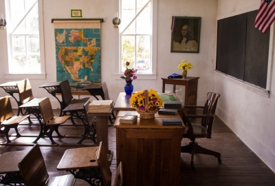 A photo of an empty classroom with an American flag next to the chalk board and a map of the United states on the wall