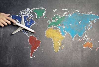 Hand guiding airplane across world map drawn on chalkboard