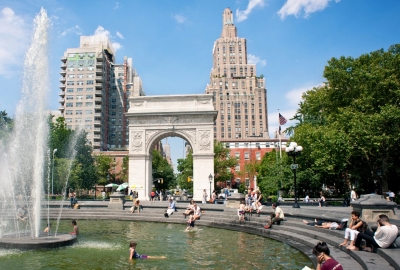 A photograph of the arch at Washington Square Park with a fountain in the foreground and people relaxing next to it