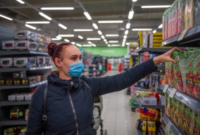 A photo of a woman wearing a face mask and grabbing juice off the shelf of a supermarket