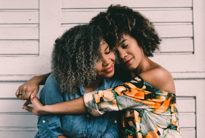 two women of color with natural hair textures hugging