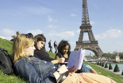 Three students are sitting on the lawn in front of the Eiffel Tower and reading a notebook