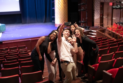 Group of six students taking a selfie in front of stage
