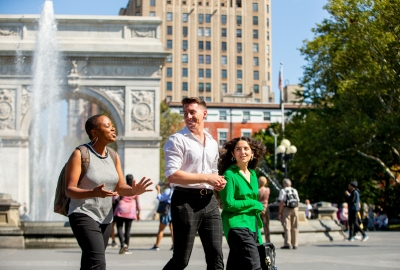 2 female and 1 male student walking, Washington Square Park Arch and fountain in the background