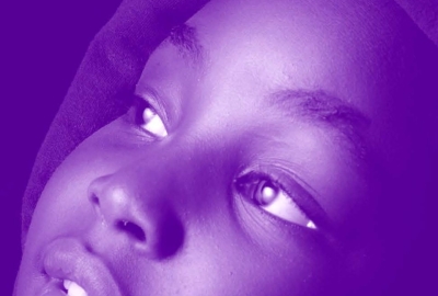 Image captures an Black child wearing a hooded sweatshirt looking off in the distance. The photo has a purple colored gaze over the entire image.