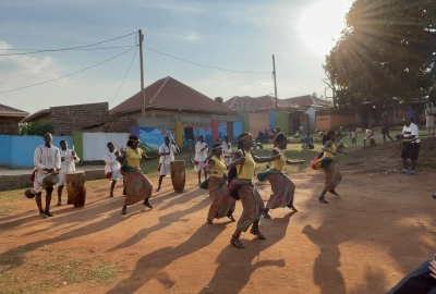 A group of Ugandan dancers perform in front of a row of buildings