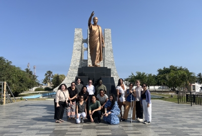 A group of students standing in front of a bronze statue of a man, in Accra, Ghana