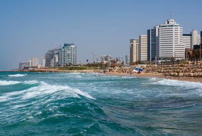 A photo of the ocean and beach in Tel Aviv, with some city buildings in the background.