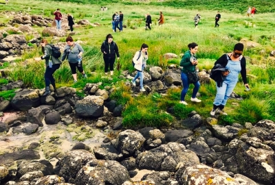 A group of students navigates a grassy hill and rocky stream by foot