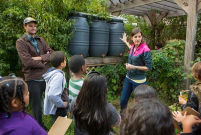 Two ECE students talking to children in front of a set of barrels.