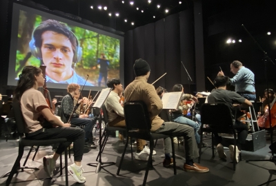 Students playing instruments in front of screen created by screen scoring students