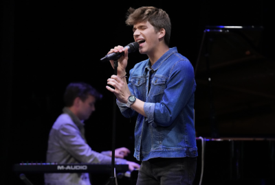 Student singing rock into the mic while piano is being played in the background