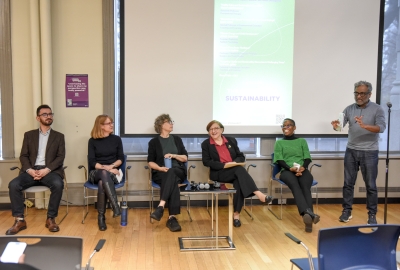 Five people sit together for a panel. One man stands and moderates.