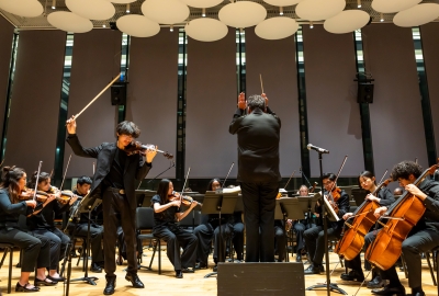 Solo violinist striking a huge stroke on the instrument while conductor leads the concert
