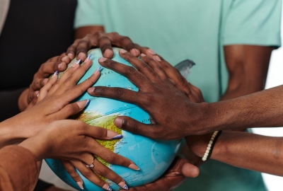 A group of students' hands are placed around a globe.