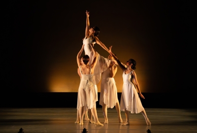 Dancers in all white holding up single dancer