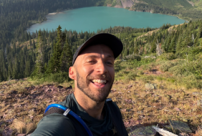 Photo of Joey Haavik hiking, body of water and mountains behind him