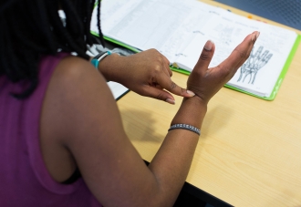 A student touching their wrist based on a diagram in a binder in front of them.