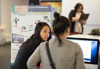 student demonstrating their work in front of a research poster and computer