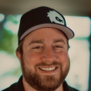 A portrait of Parker Lynch in a v-neck shirt and baseball cap with logo on it.