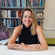 white woman with long hair in a black top sitting at a desk in front of books
