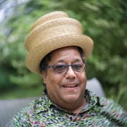 A photo portrait of Scott Alves Barton with a straw hat and a green flowered shirt.