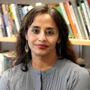 A portrait of Paula Chakravartty wearing a gray blouse in front of a bookcase.