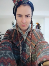 me dressed in a coat with geometric patterns, with two long braids sticking out of the scarf wrapped around my head. I'm looking right at the viewer, slightly and cunningly smiling
