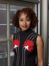 Dr. Nicole R. Fleetwood stands next to a window wearing a black dress with white stripes and red flowers.