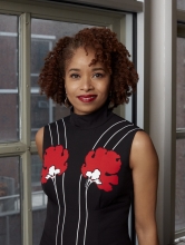 Dr. Nicole R. Fleetwood stands next to a window wearing a black dress with white stripes and red flowers.
