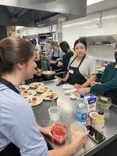 Two students speak to one another as they prepare multiple plates of pureed food for individuals with swallowing problems. 
