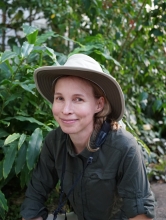 Haley Mellin, in an outdoors hat and green shirt, smiles against a backdrop of tropical foliage. 