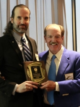 Justin Tausig poses with a plaque and an organization official at his USA Fencing Hall of Fame induction.