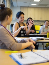 A woman in an occupational therapy classroom points to her hand to illustrate an exercise.