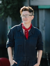 Half-body portrait photograph of Laine Nooney in a blue jumpsuit with a red bandana around their neck.