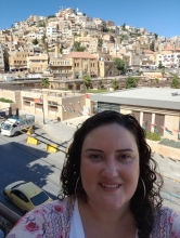 A white woman with curly brown hair standing in front of a hillside city